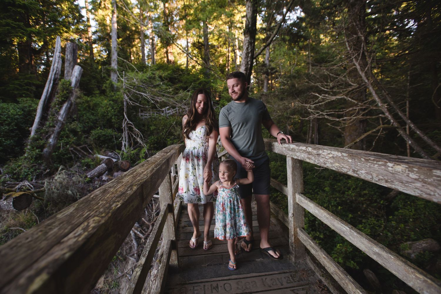 Family enjoying a peaceful moment together on a rustic wooden bridge surrounded by lush forest scenery.