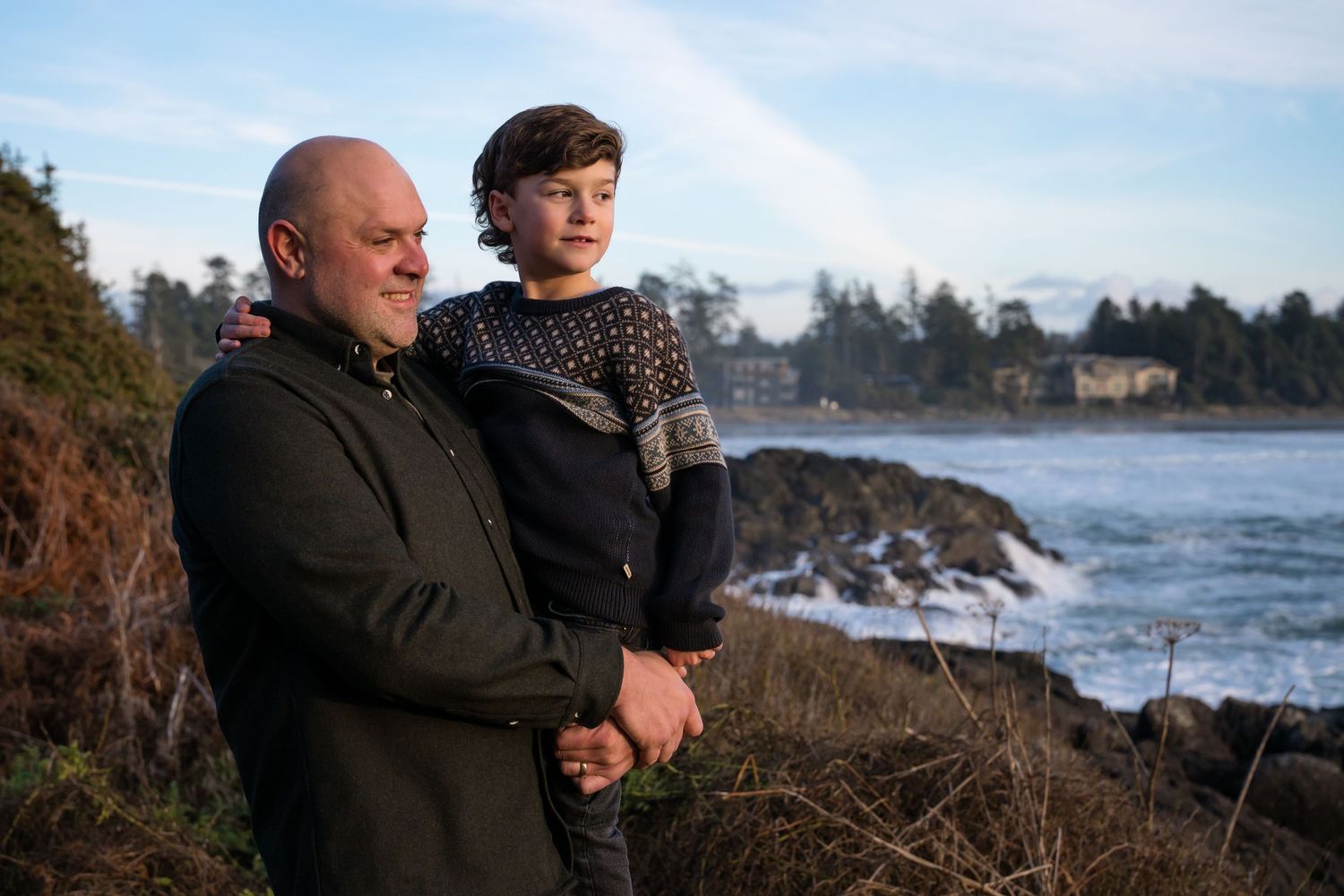 Family enjoying a scenic coastal view together on a rocky beach with evergreen trees in the background.