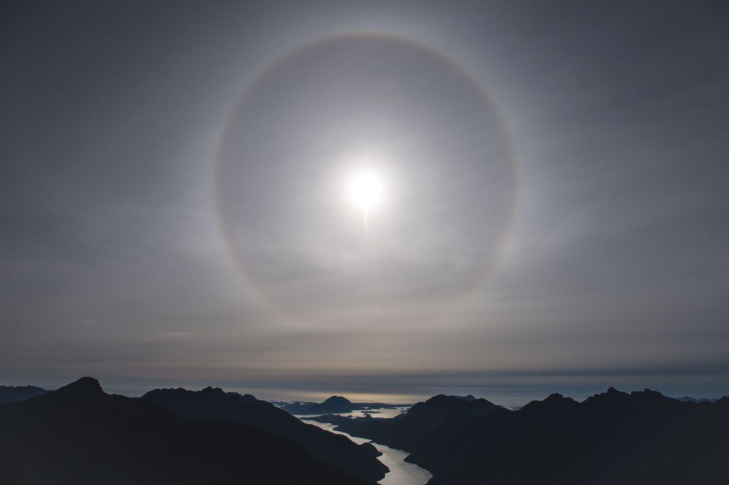 Stunning sun halo phenomenon creates a circular rainbow effect in the cloudy mountain sky.