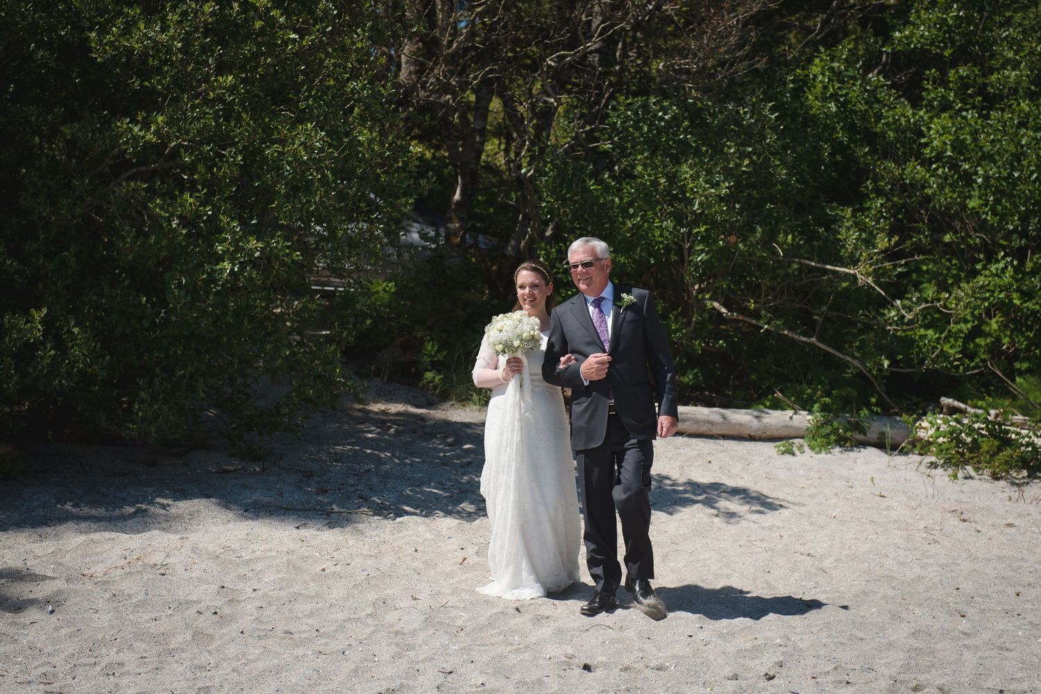 Outdoor wedding ceremony taking place on a sunny beach with natural greenery.