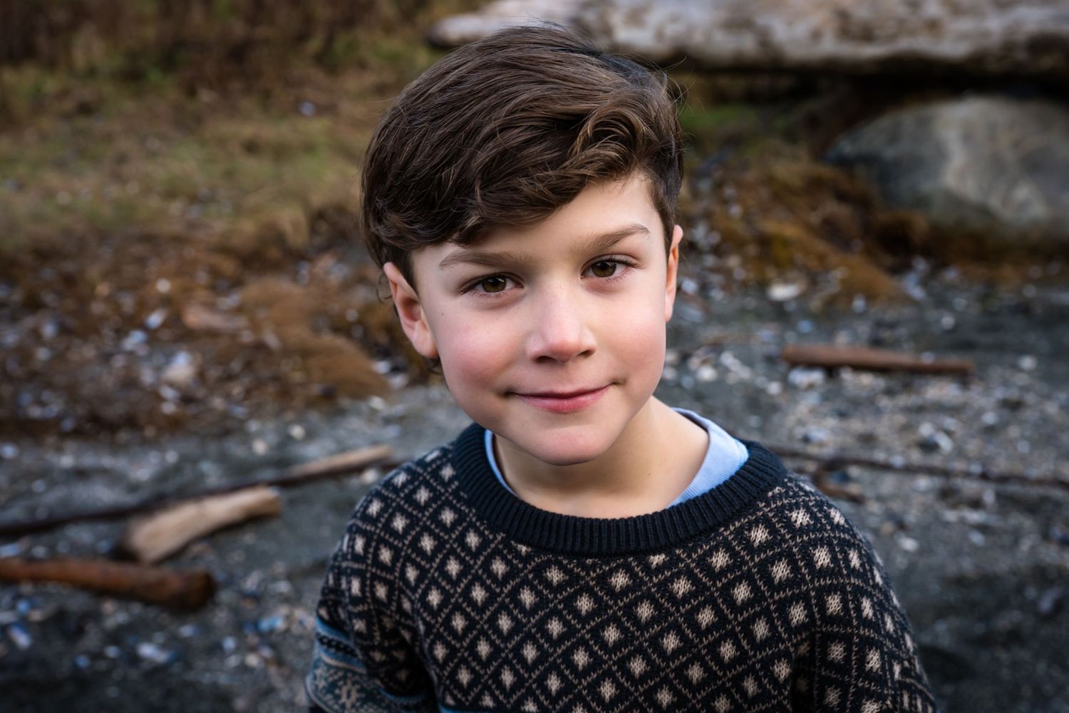 Child wearing a patterned sweater smiles while enjoying an outdoor adventure by the coast.