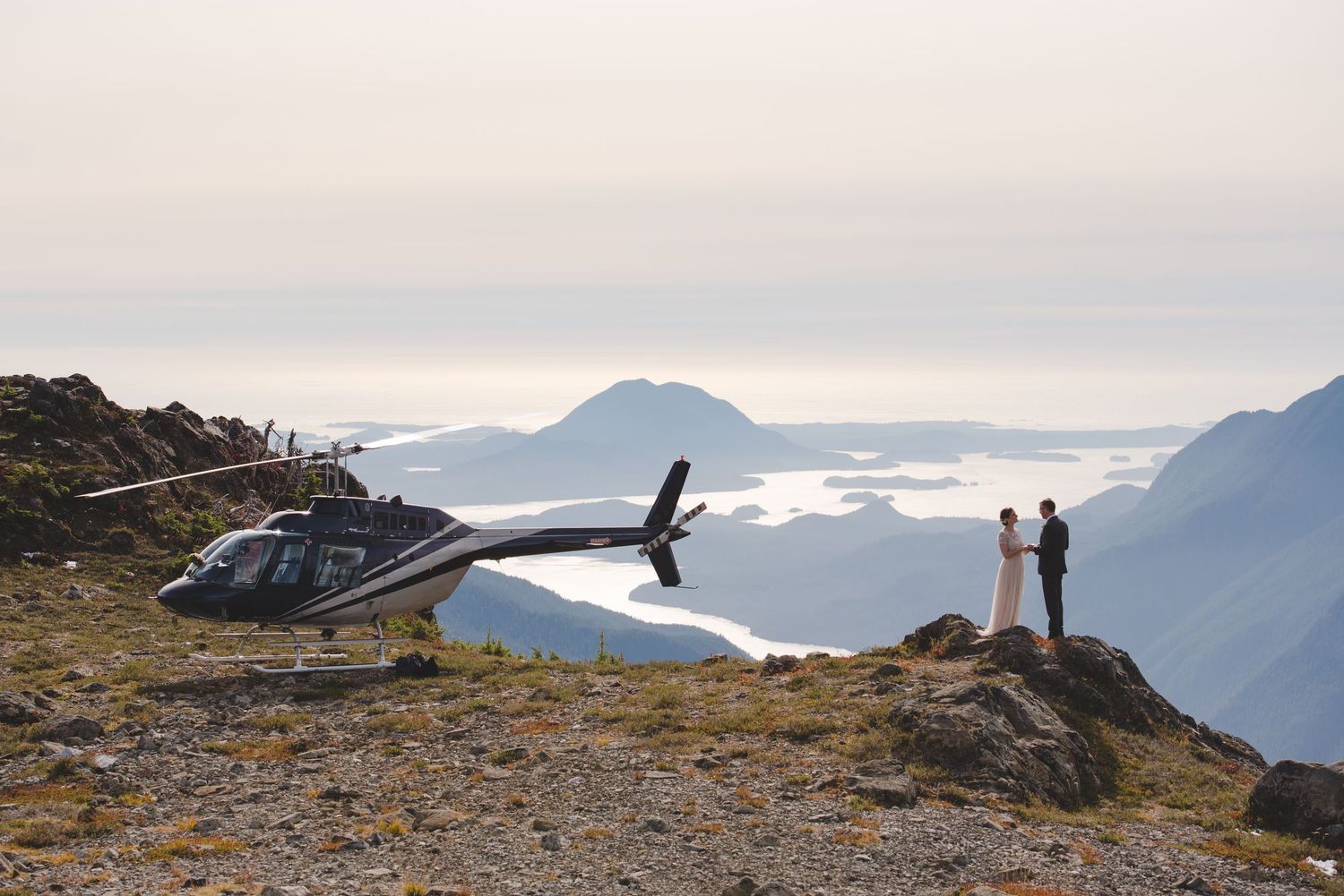 Helicopter wedding photo session on a mountain peak overlooking coastal mountains.