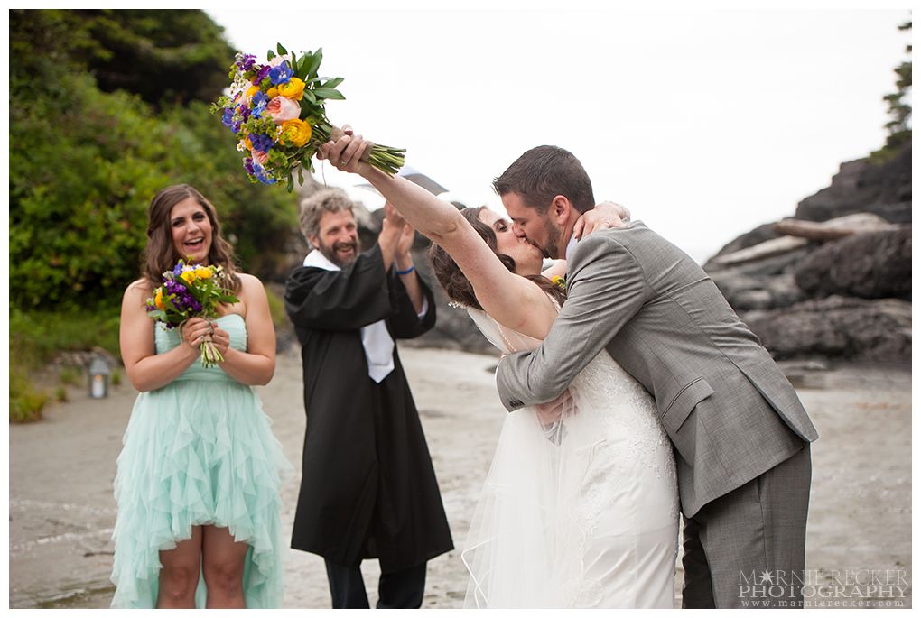 Wedding party celebrating with colorful bouquets on rocky beach.