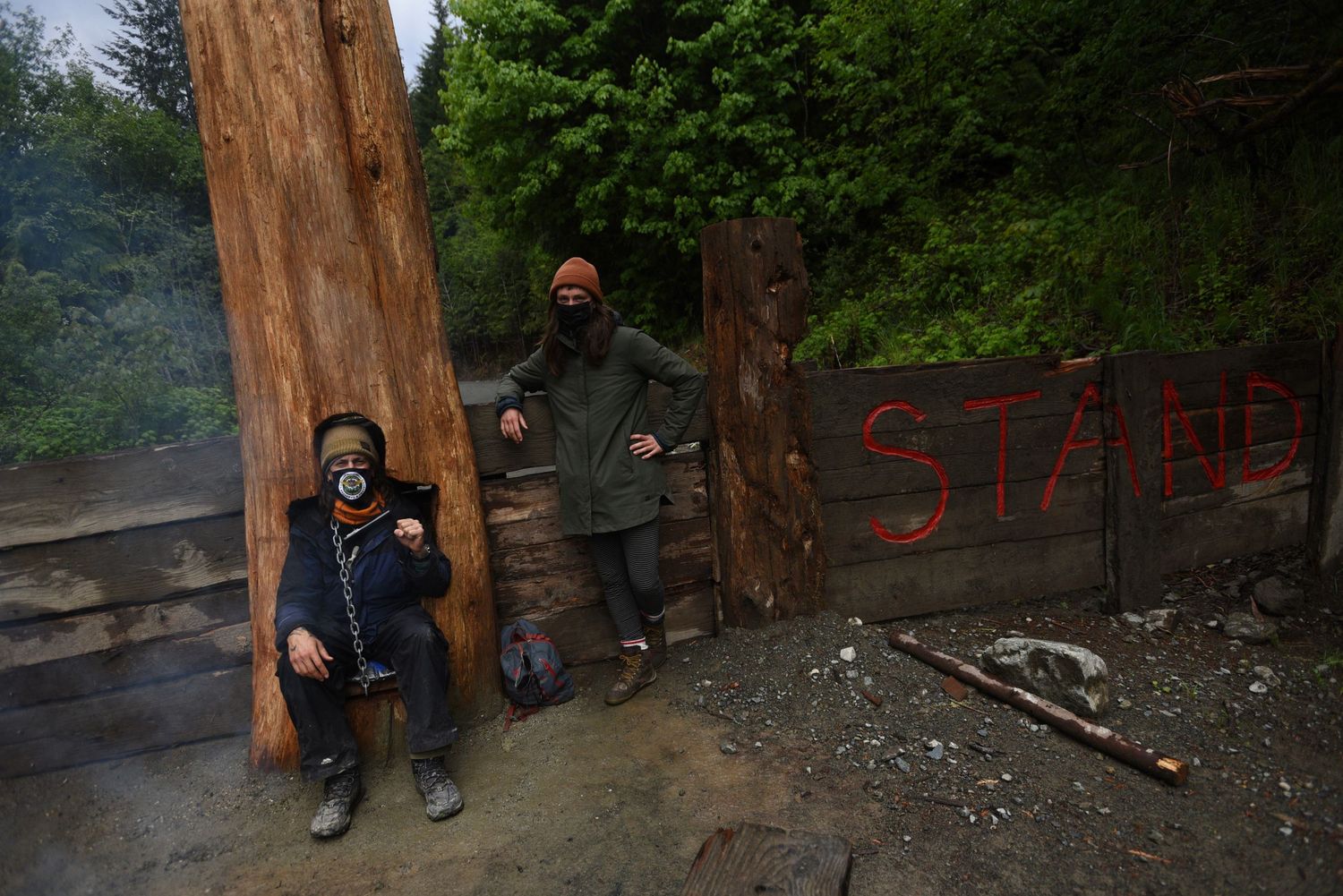 Fairy Creek blockade. People stand along a dirt path in a wooded area near large tree trunks.