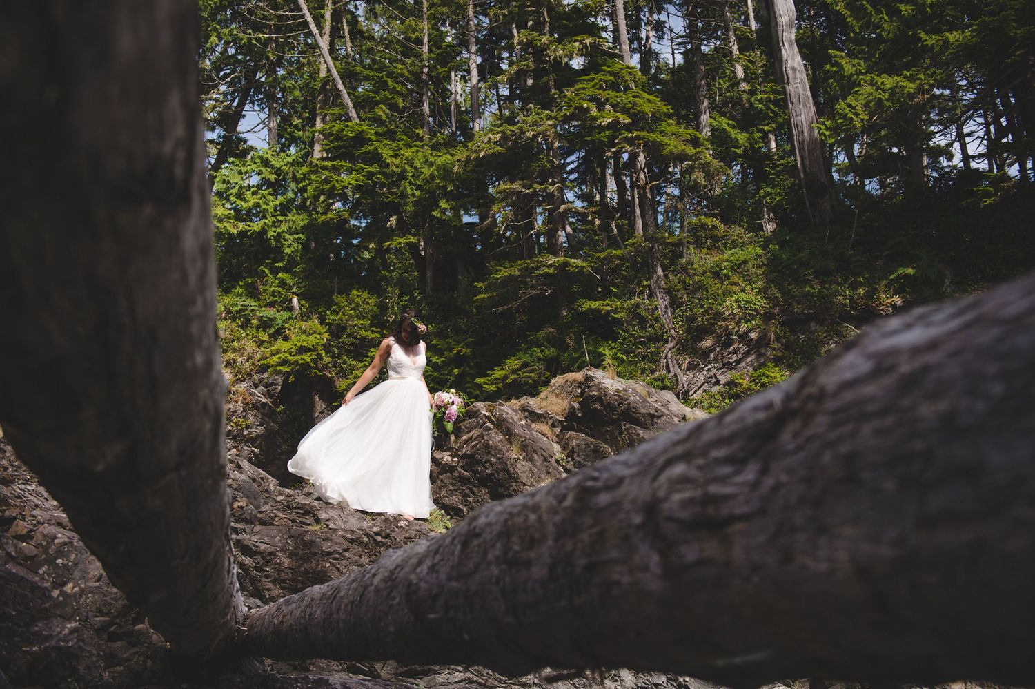 A flowing white wedding dress contrasts against dark forest rocks and trees.