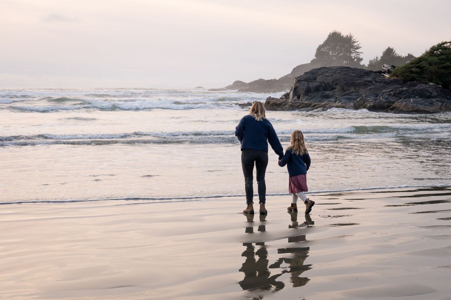 Family walking along the water's edge at a foggy coastal beach.