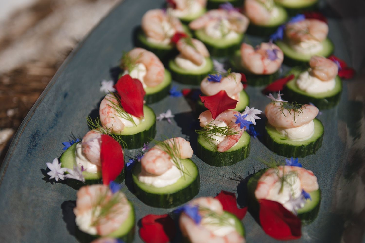 Elegant appetizers with cucumber slices garnished with flowers on a dark platter.