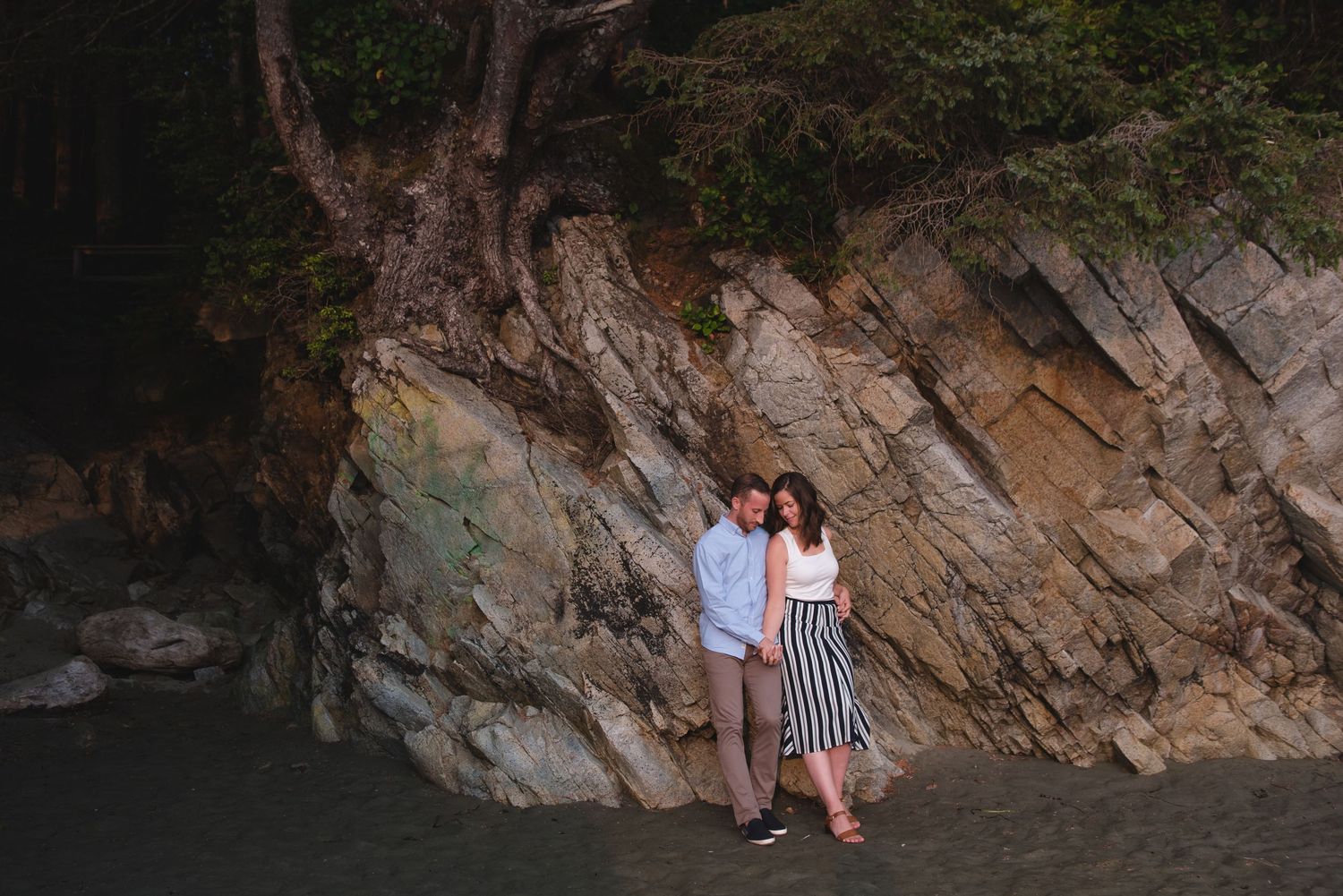 Romantic couple embraces near rocky cliffside during sunset photo session.