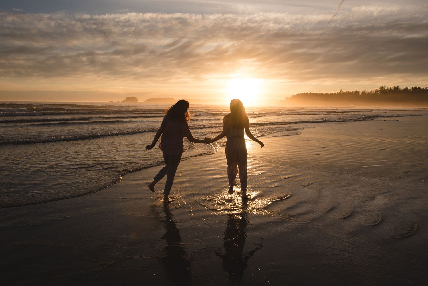 Silhouettes of people walking on beach at sunset with golden light reflecting on wet sand.
