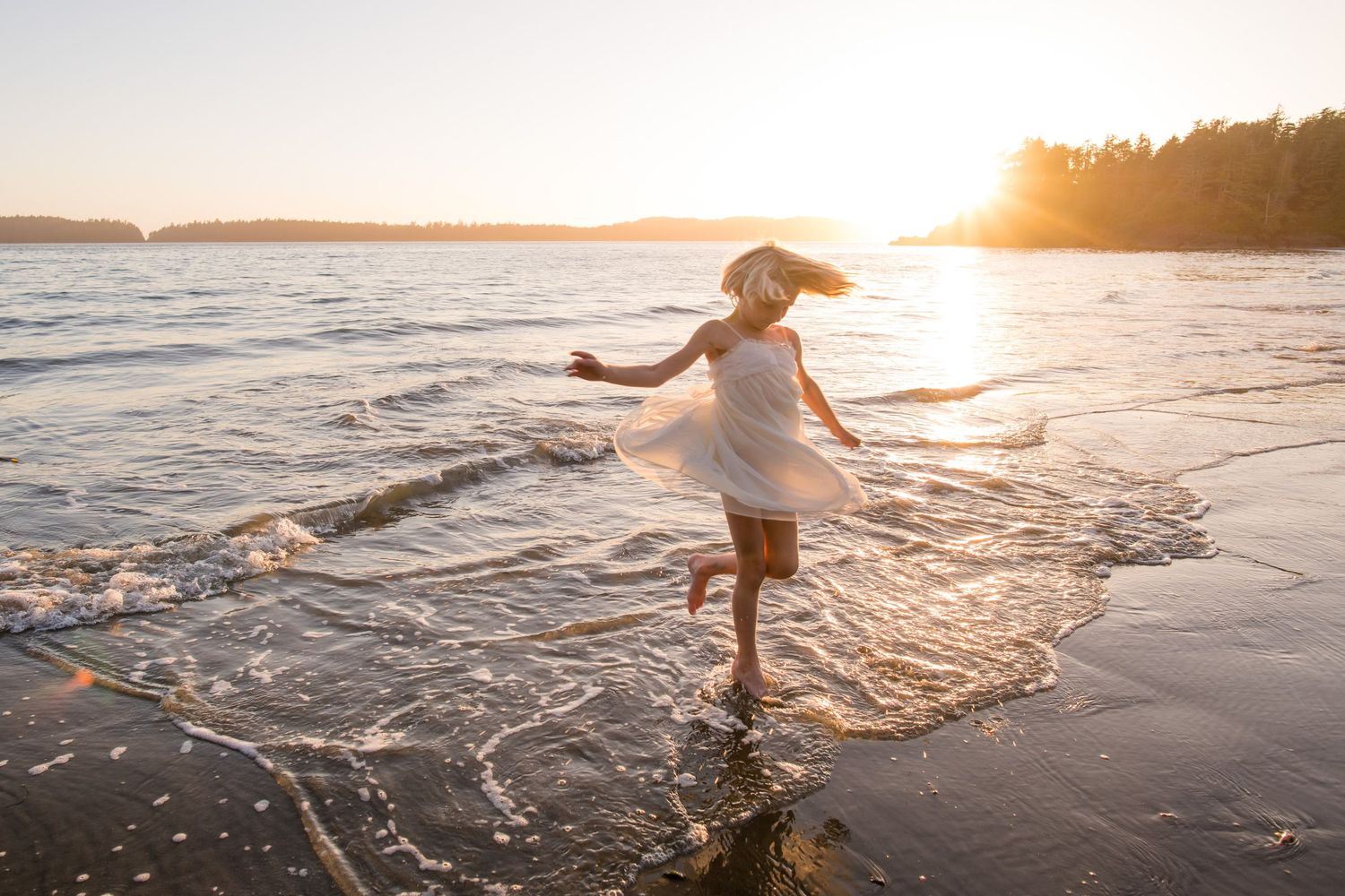 A person splashes through shallow ocean water at sunset creating a magical silhouette against the golden sky.
