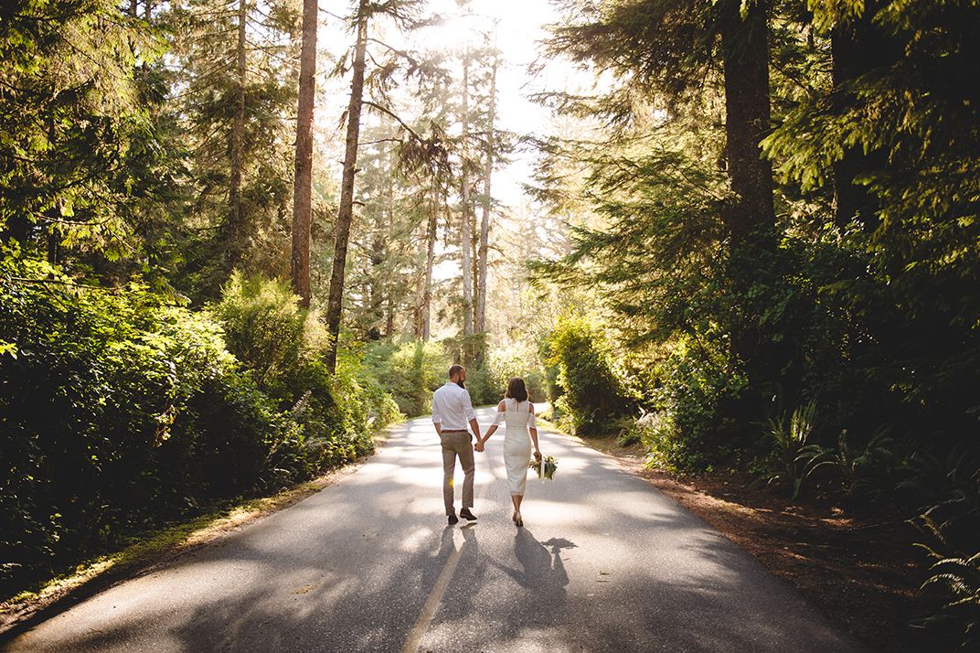 Sun-dappled forest path lined with tall evergreen trees creates a natural wedding aisle.