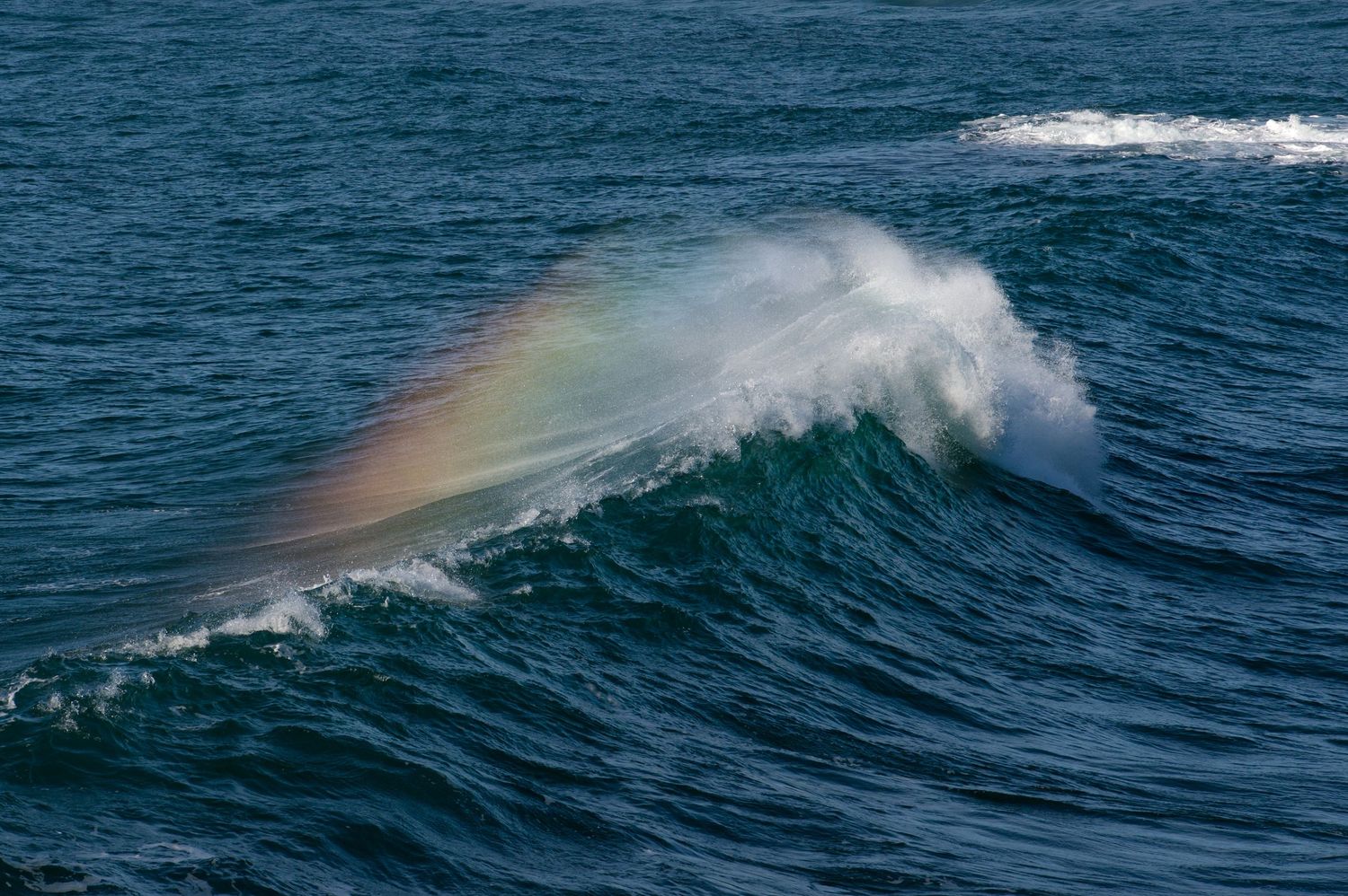 Ocean waves create a misty rainbow spray against deep blue waters.