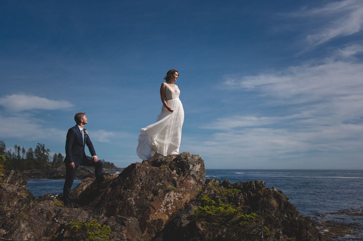 Wedding couple explores rocky coastal cliffs with ocean views on their special day.
