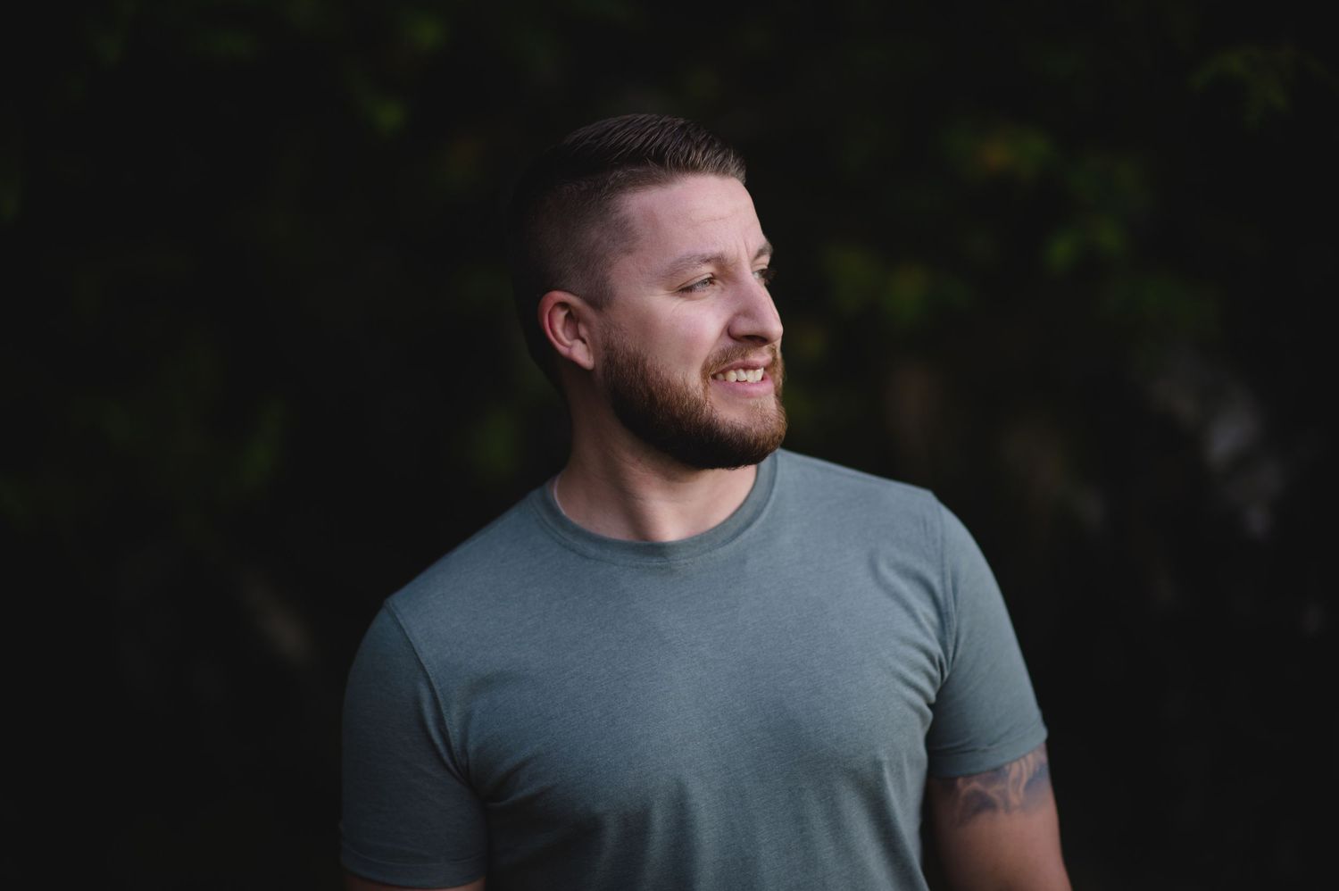 A person in a gray t-shirt stands against a dark background.