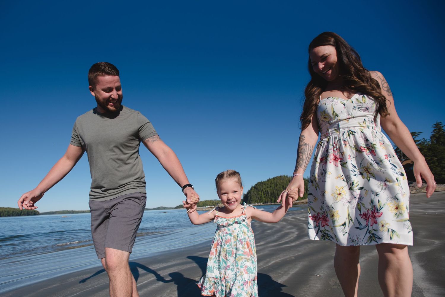 Family enjoying playful moment together on sunny beach with ocean backdrop.