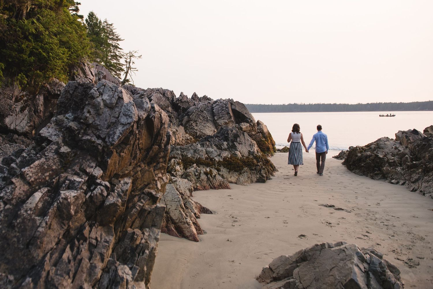 Two people walk along a scenic coastal beach path with rocky cliffs and ocean views at sunset.