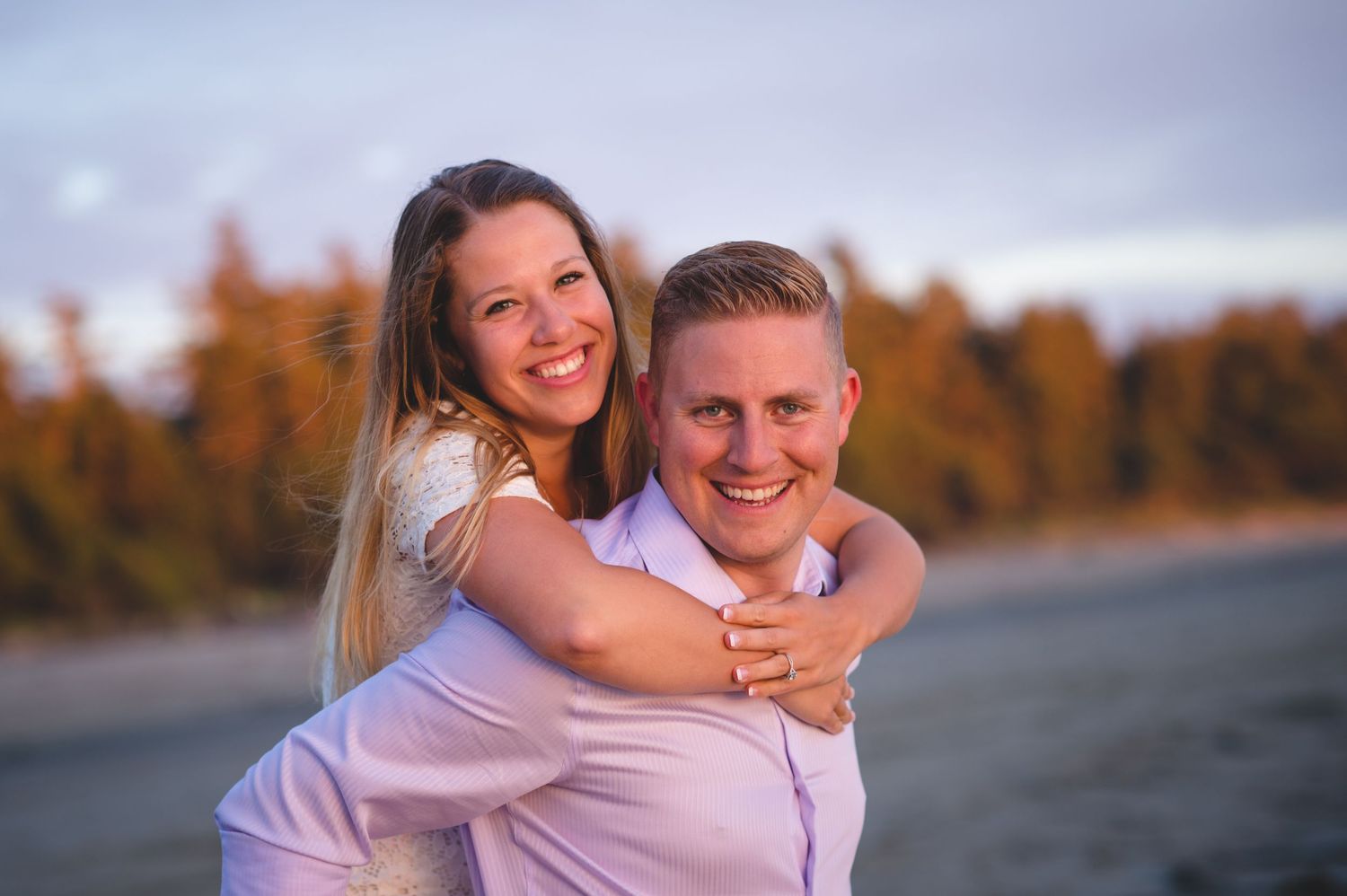 A couple embraces outdoors during sunset with autumn foliage in the background.