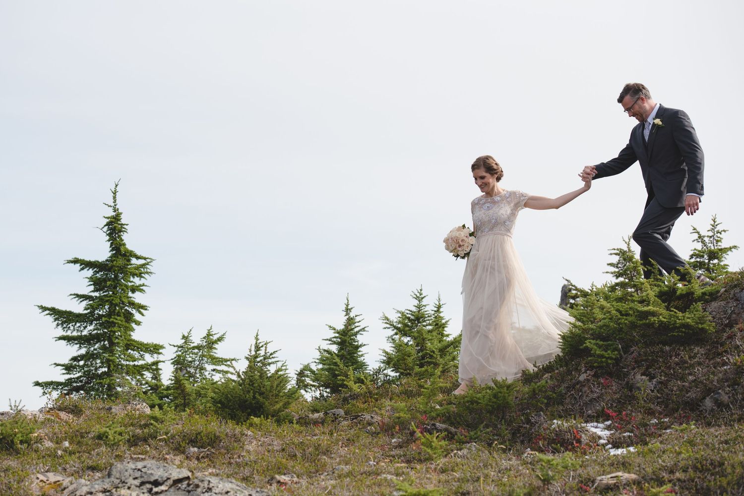 A couple navigates rocky terrain during their adventurous mountain wedding photoshoot.