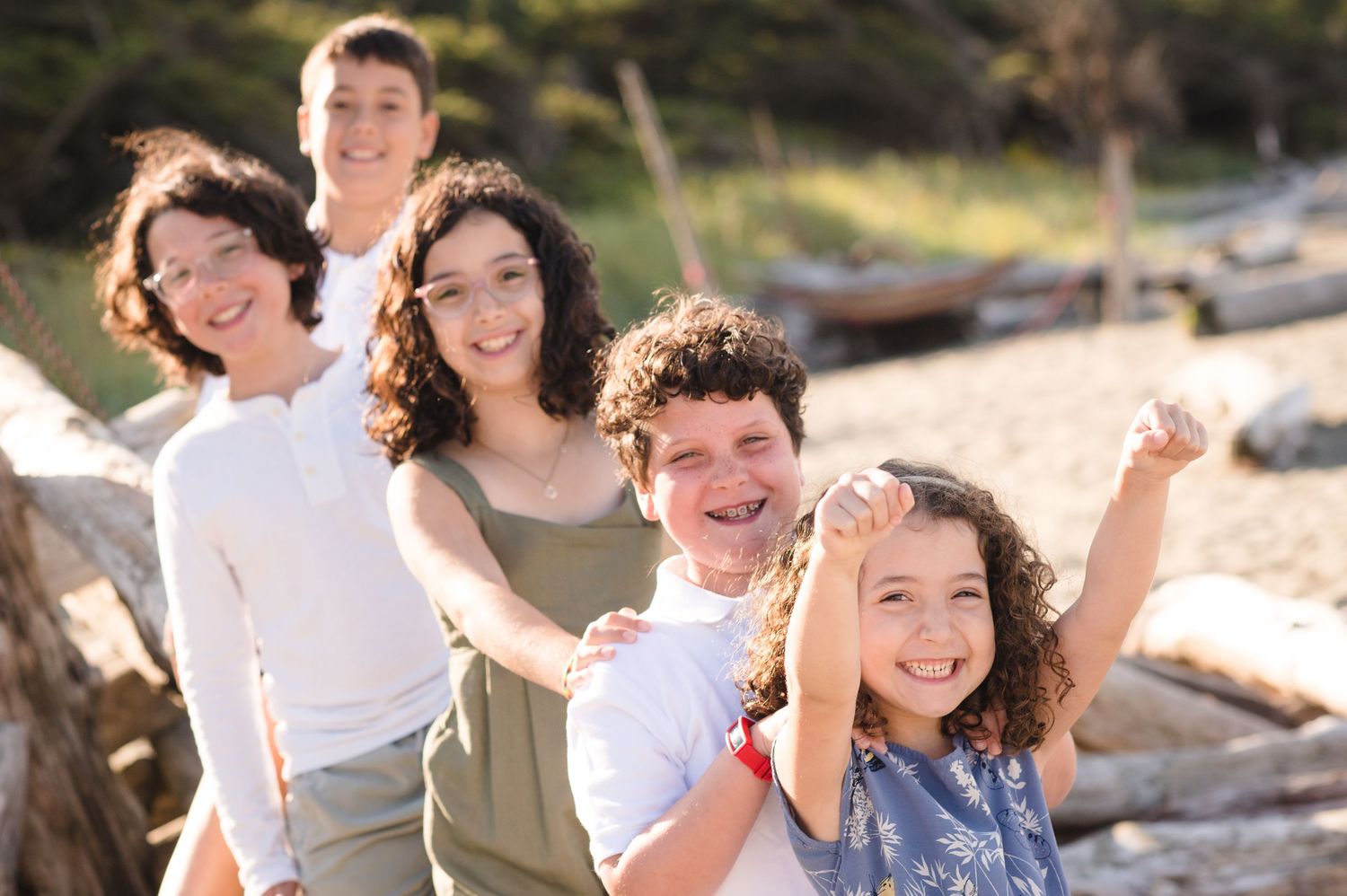 Joyful family photo session with everyone laughing together on beach driftwood.