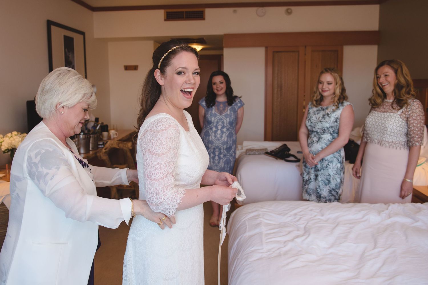 A group of people in formal attire gather in a room during wedding preparations.