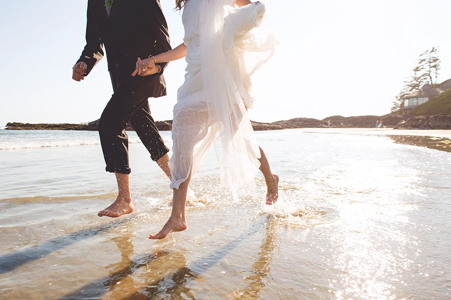 Joyful wedding party splashing in ocean waves at sunset.