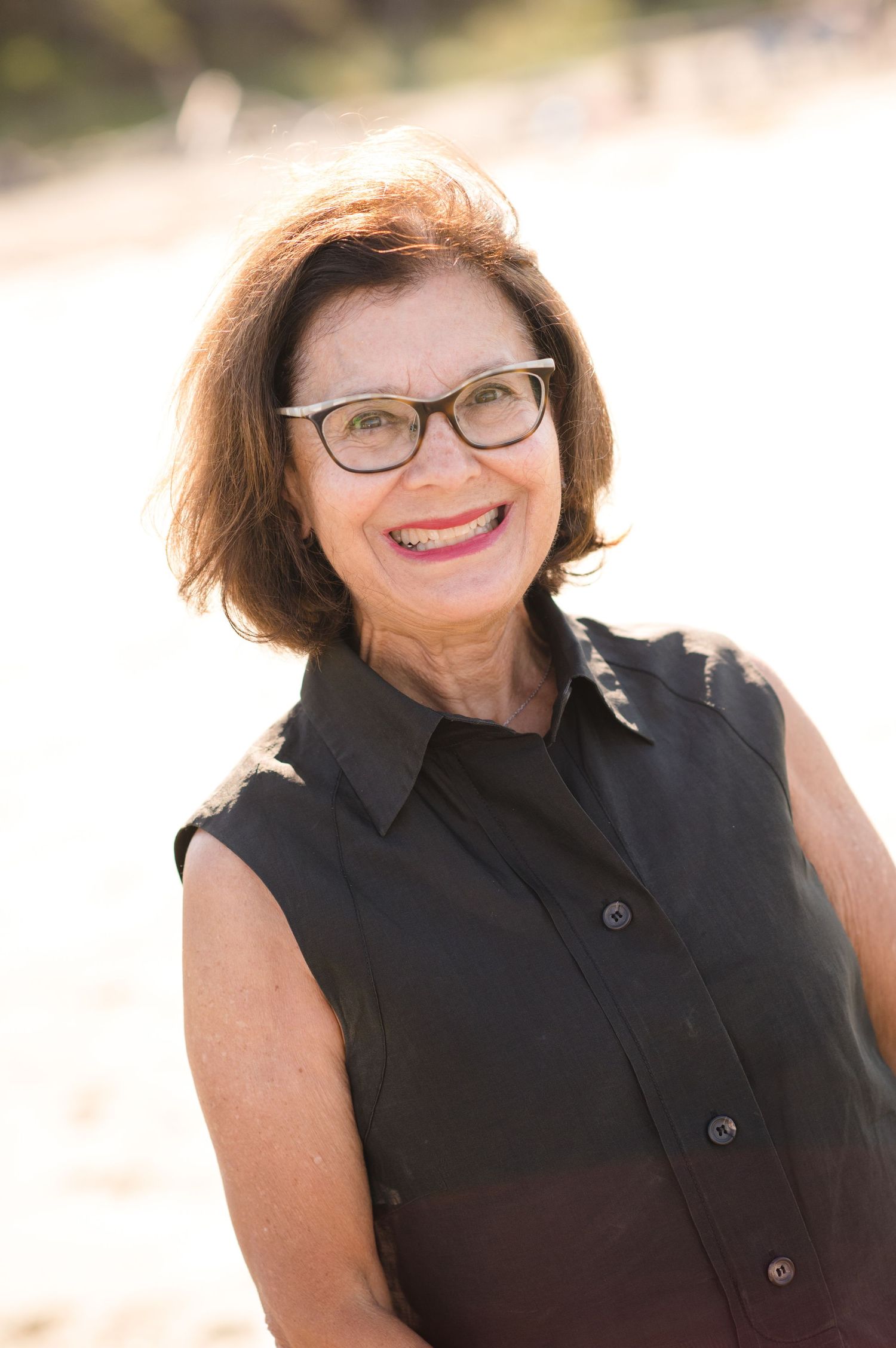 Portrait series of a woman in black sleeveless top smiling against beach backdrop.