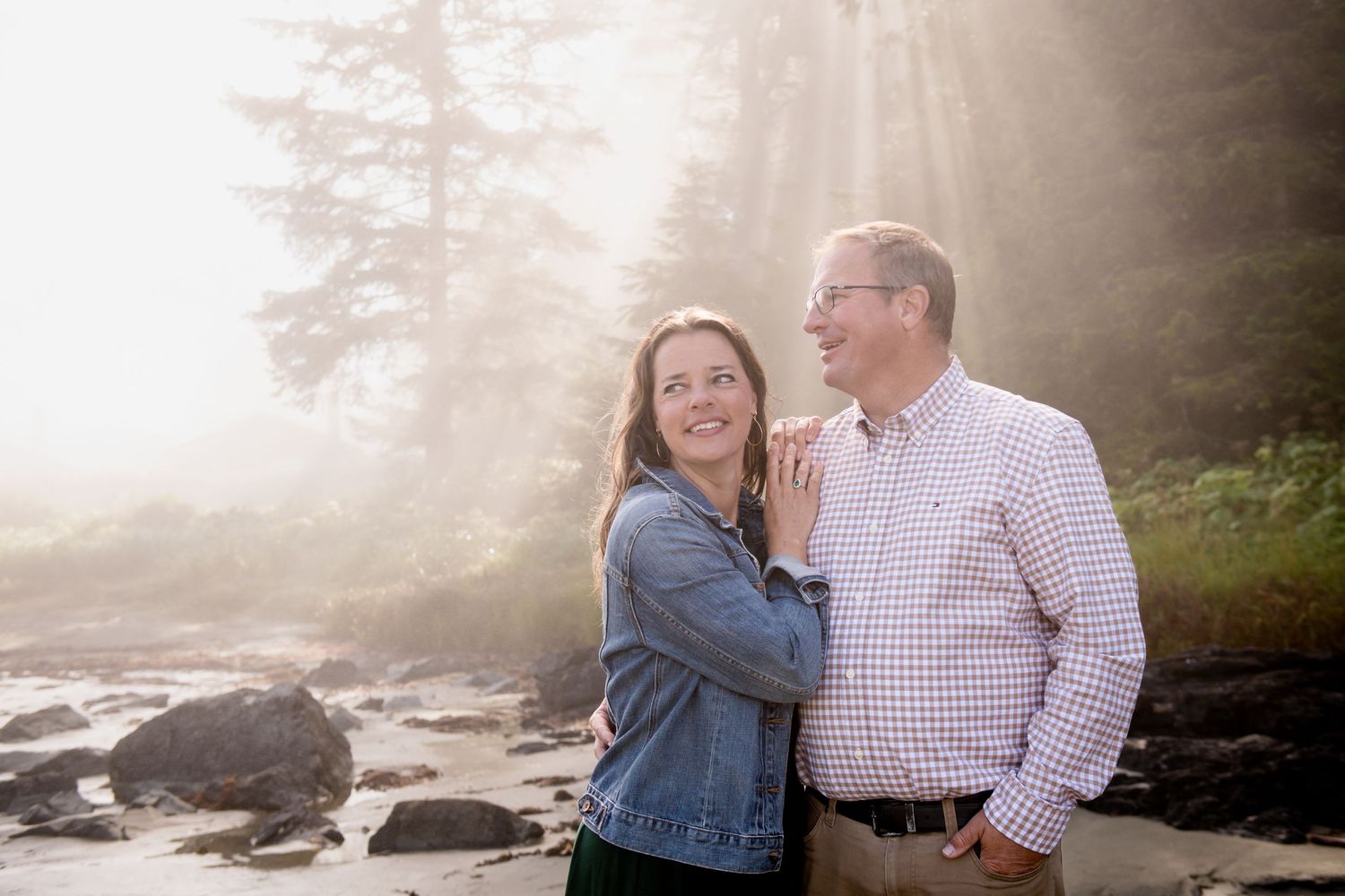 Couple embracing in dreamy sunlit forest setting during photo session.