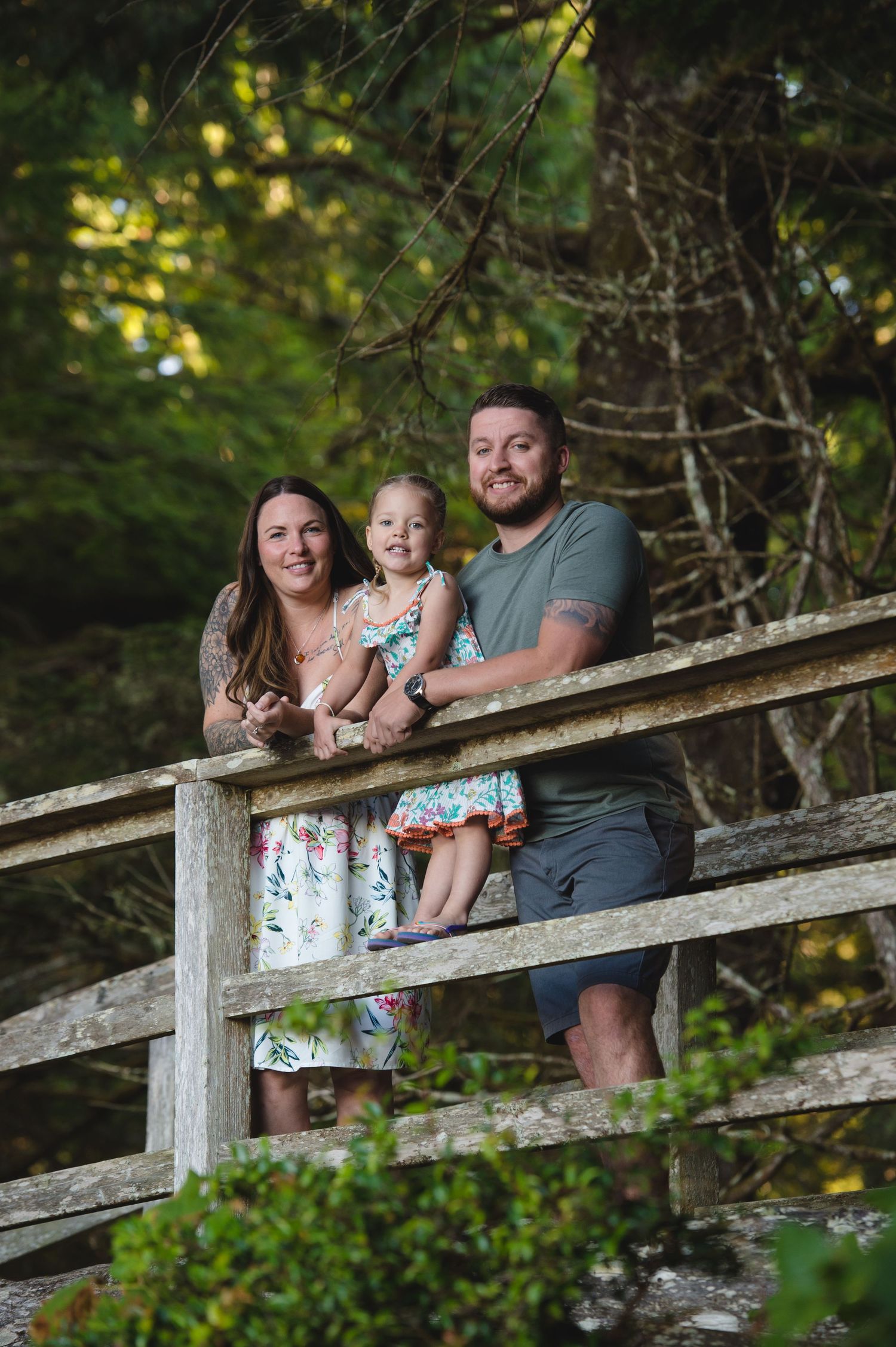 Family relaxing together on rustic wooden bridge railing surrounded by green foliage.