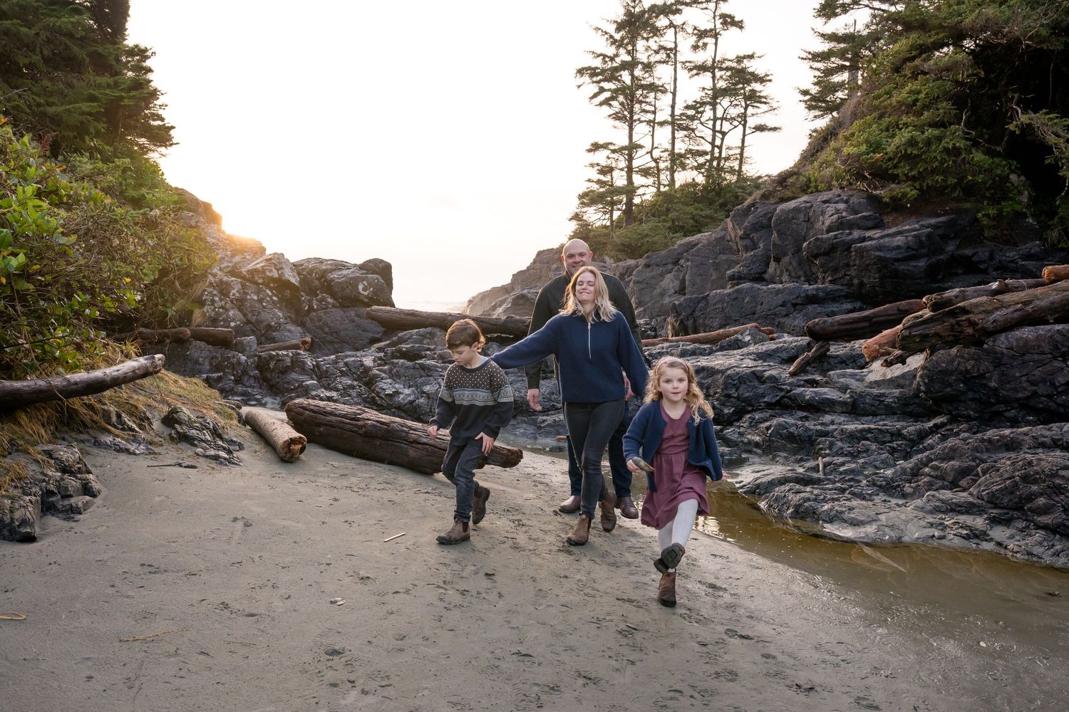 Family walking along the rugged coastline during golden hour with evergreen trees in the distance.