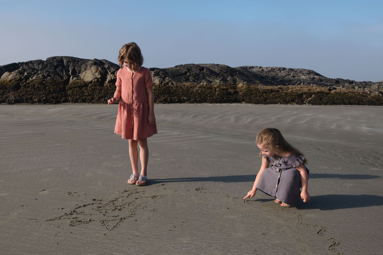 Children drawing shapes in the wet sand on a peaceful beach during sunset.