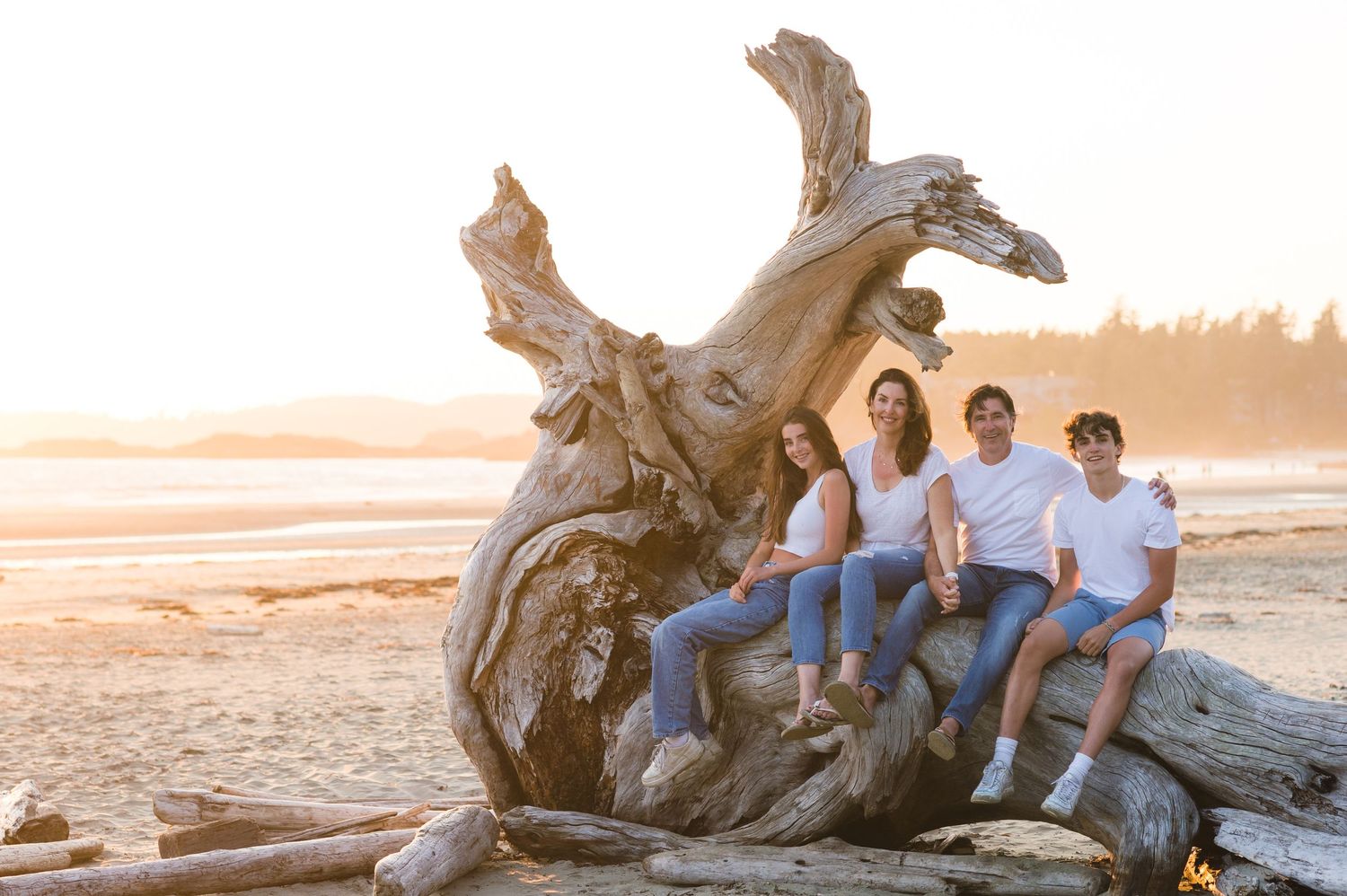 A group sits together on driftwood at a scenic beach during sunset.