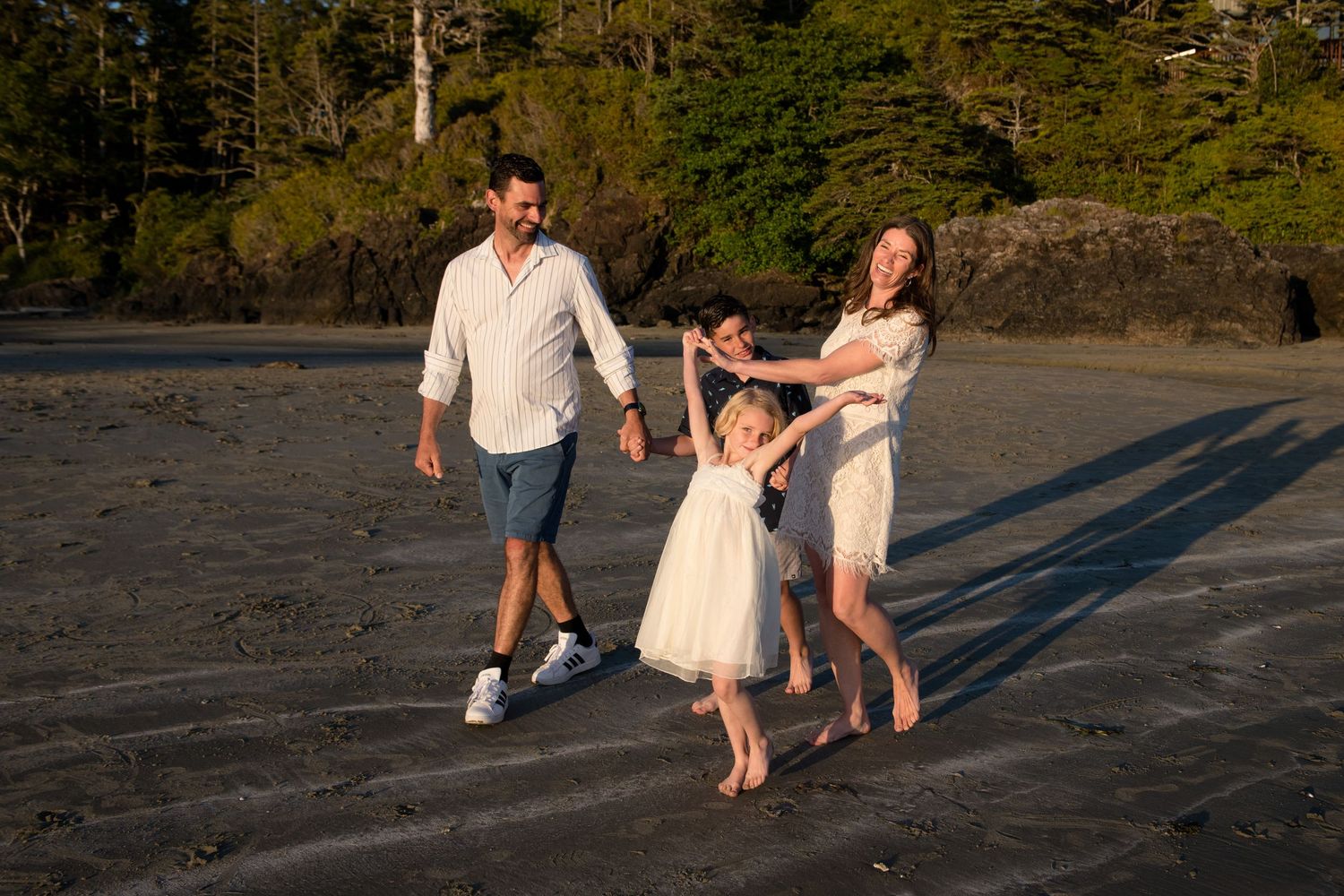 People play and dance together on a beach at golden hour casting long shadows on the sand.