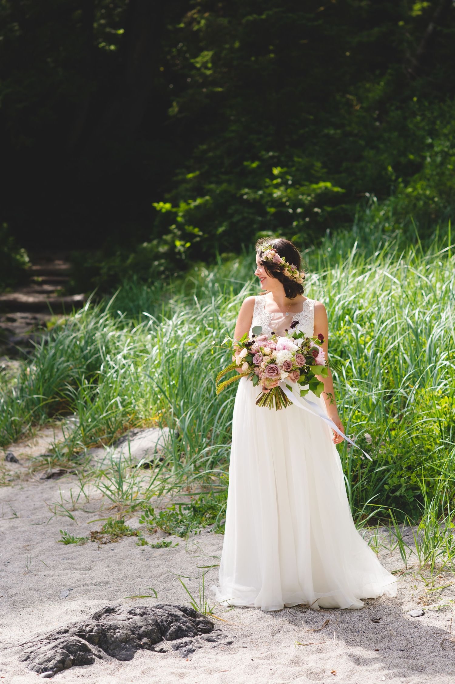 Wedding photography session on a sandy beach with tall grass and natural rock formations.
