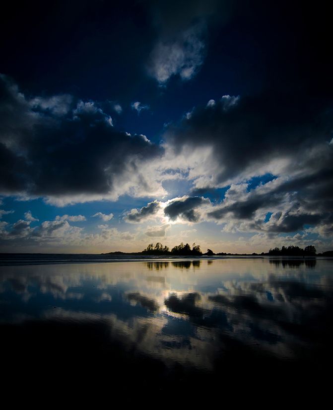 Dramatic sunset sky reflects perfectly in still waters creating a mirror-like panoramic view.