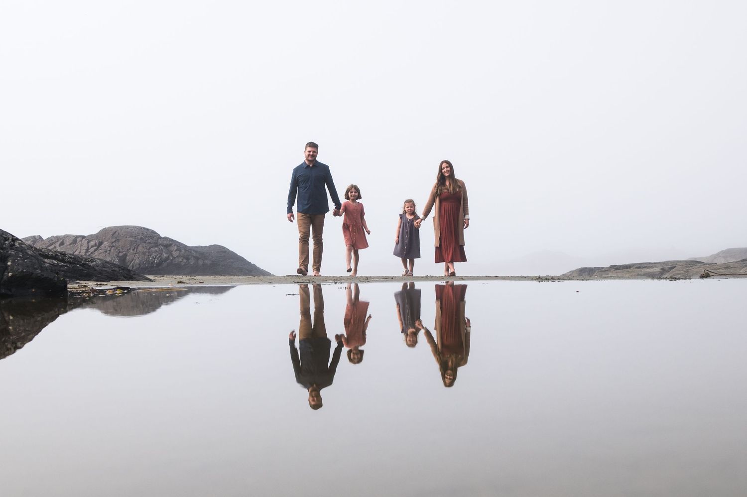 Family enjoying peaceful walk along misty Pacific Northwest beach with mountain views.