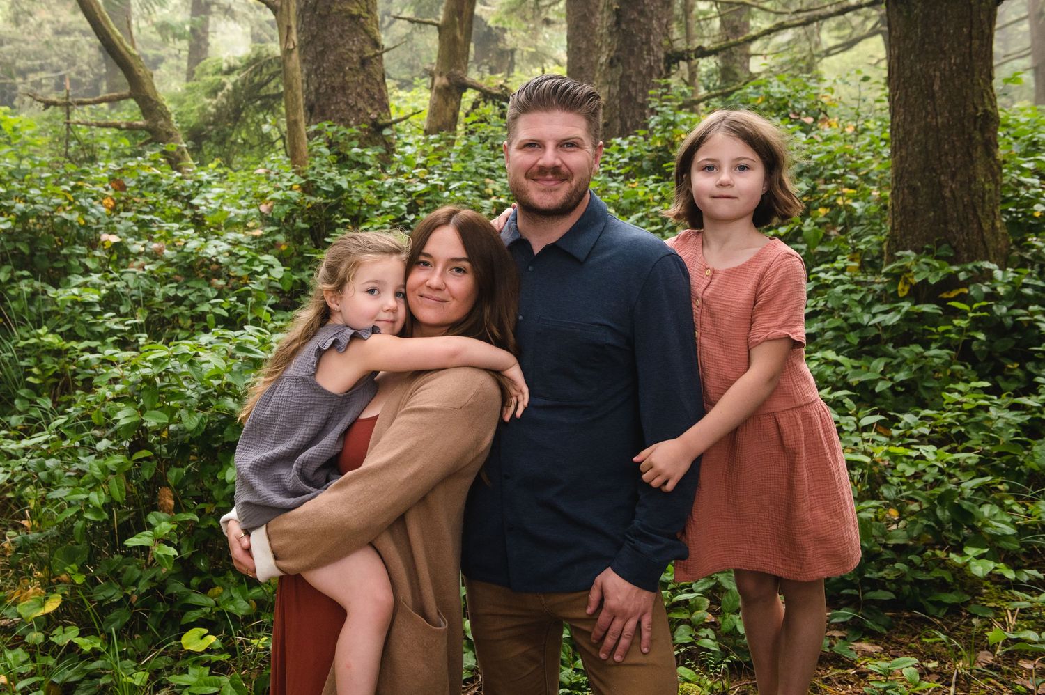 Family gathering for portraits among towering trees in a forest clearing.