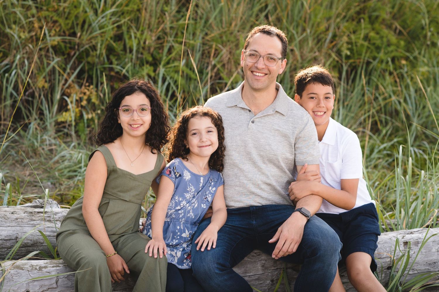 Group photo of family members sitting together on weathered beach logs against coastal vegetation.