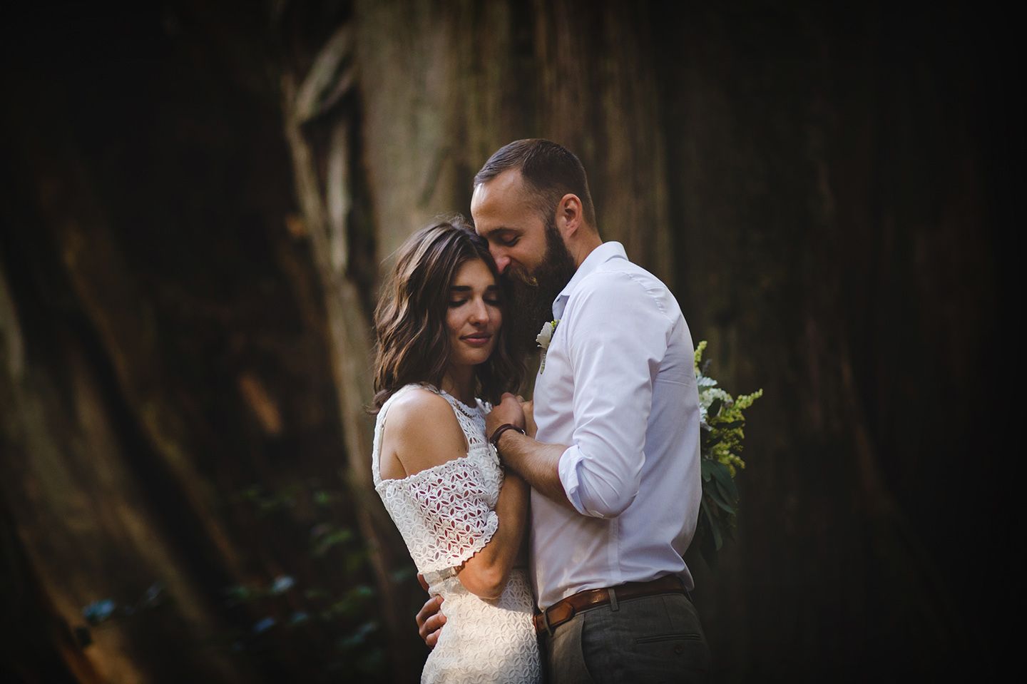 Intimate wedding moment captured in a dark, moody forest setting.