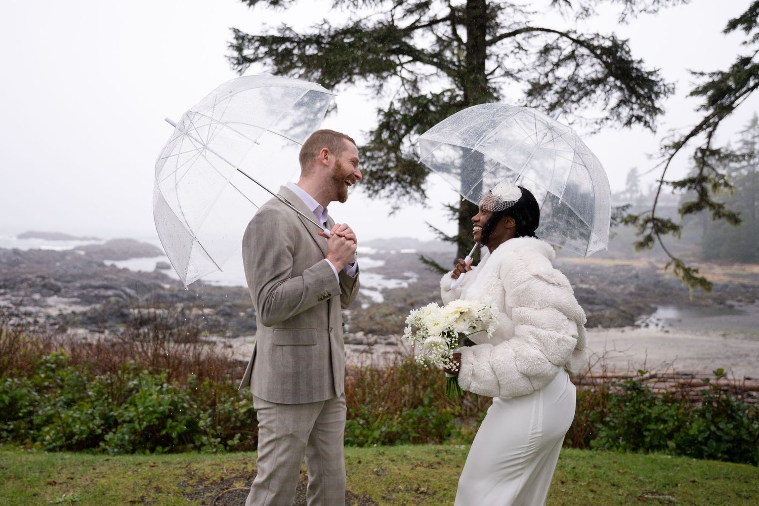 A romantic wedding couple shares an intimate moment under umbrellas in a misty mountain landscape.