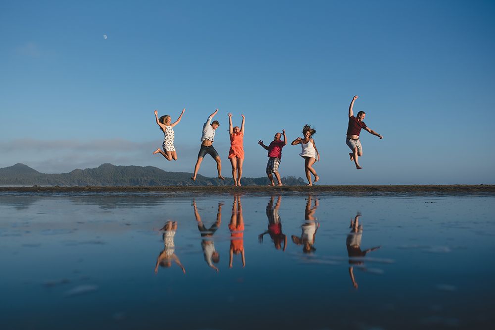 Group of people jumping into the air in sequence against a scenic lake and mountain backdrop.