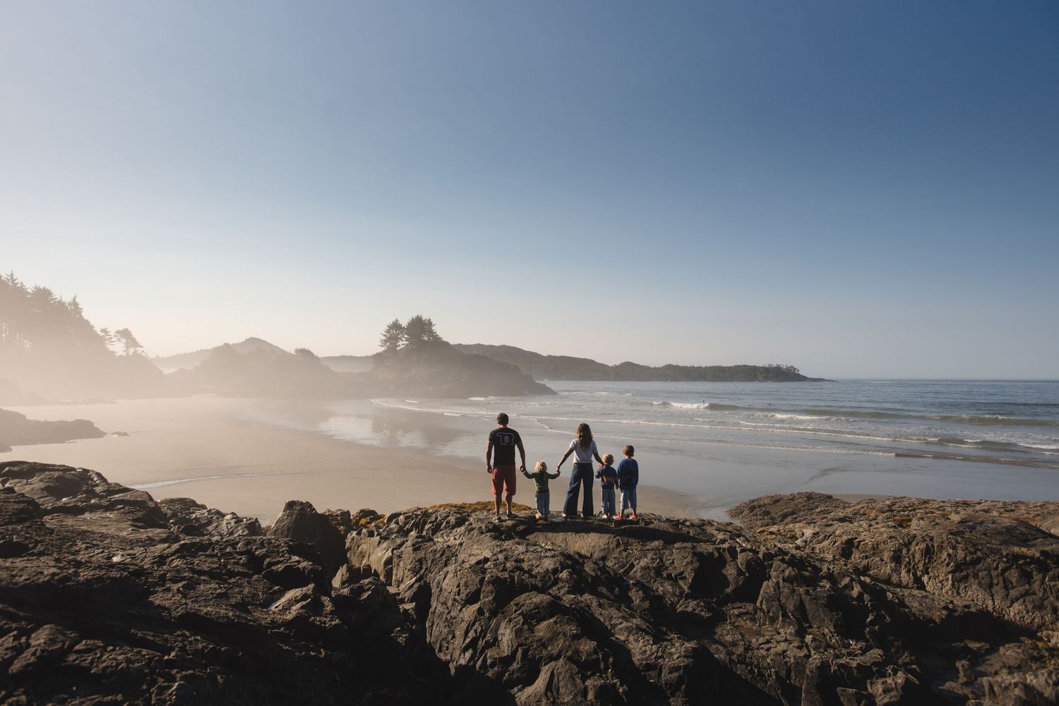 Silhouettes of people walking along a rocky Pacific Northwest coastline at sunset.