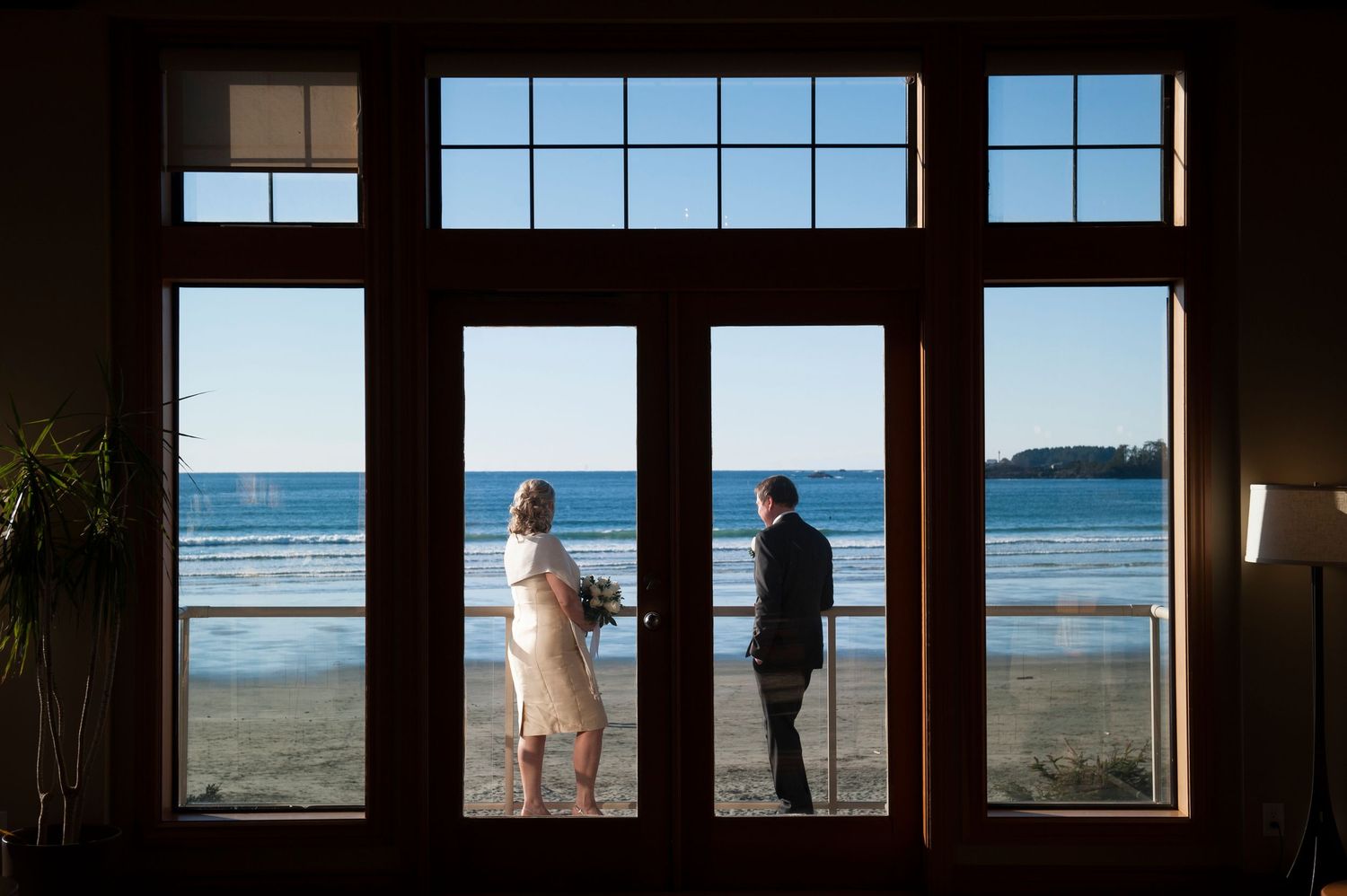 Scenic ocean view framed through large windows with figures in silhouette.