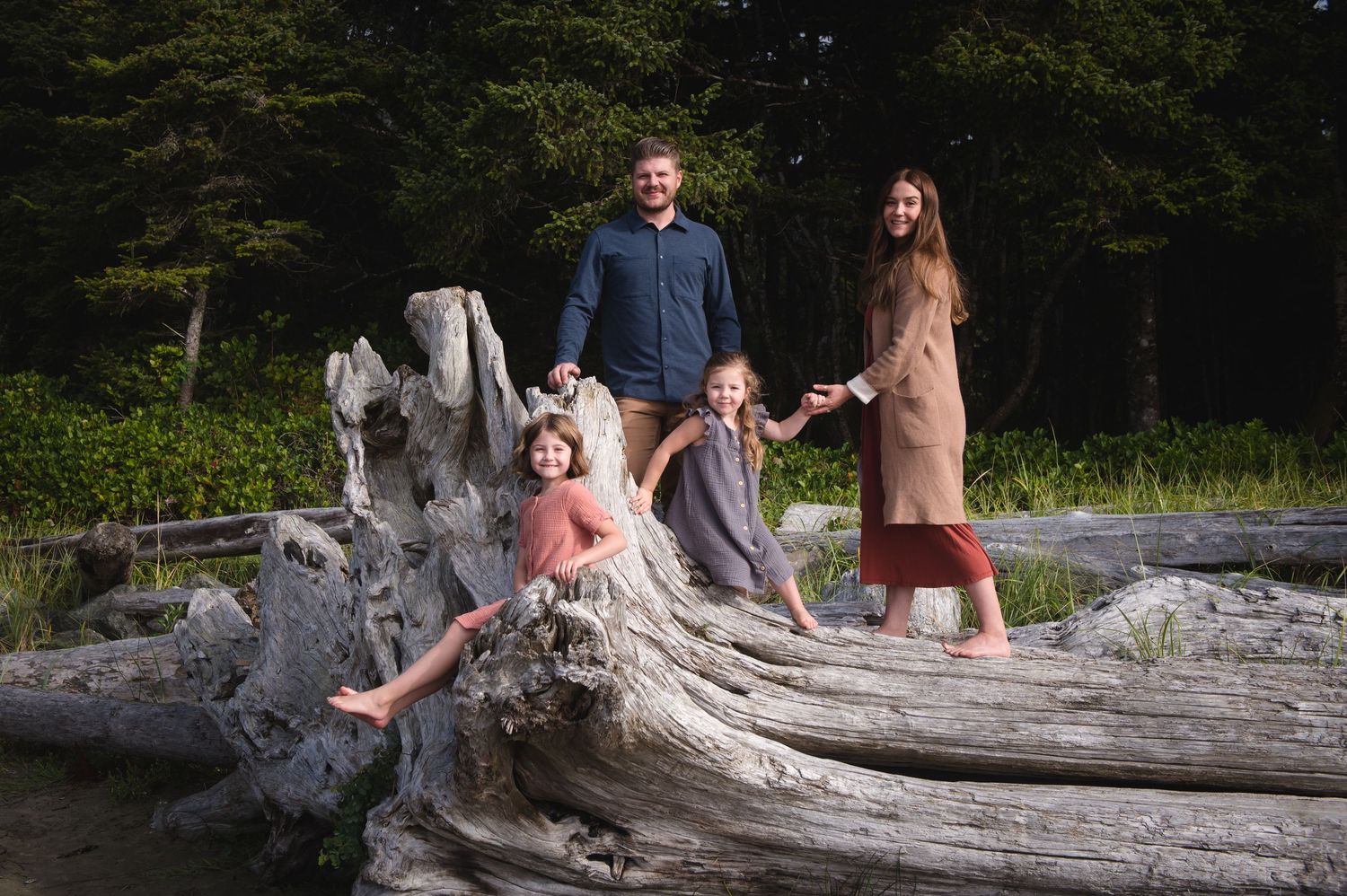 A group poses together on a large piece of driftwood at the beach.