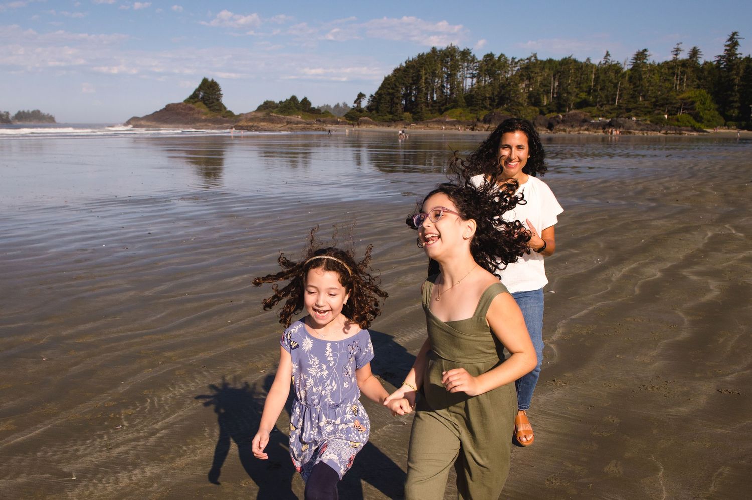 Playful family interactions on wet sand beach with forested coastline in background.