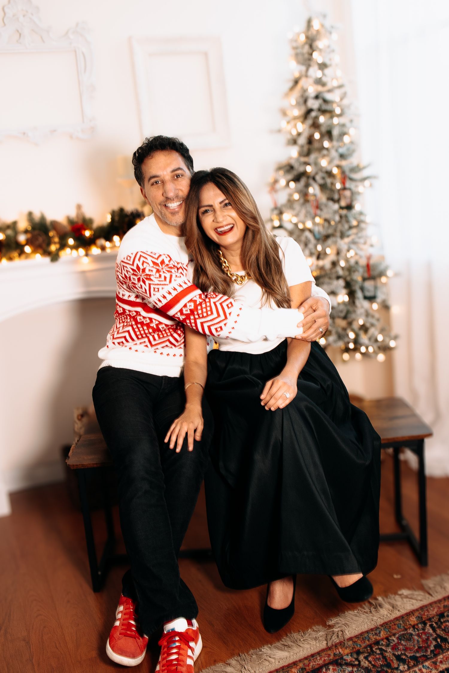 Couple in coordinated holiday outfits sitting together in front of decorated Christmas tree.