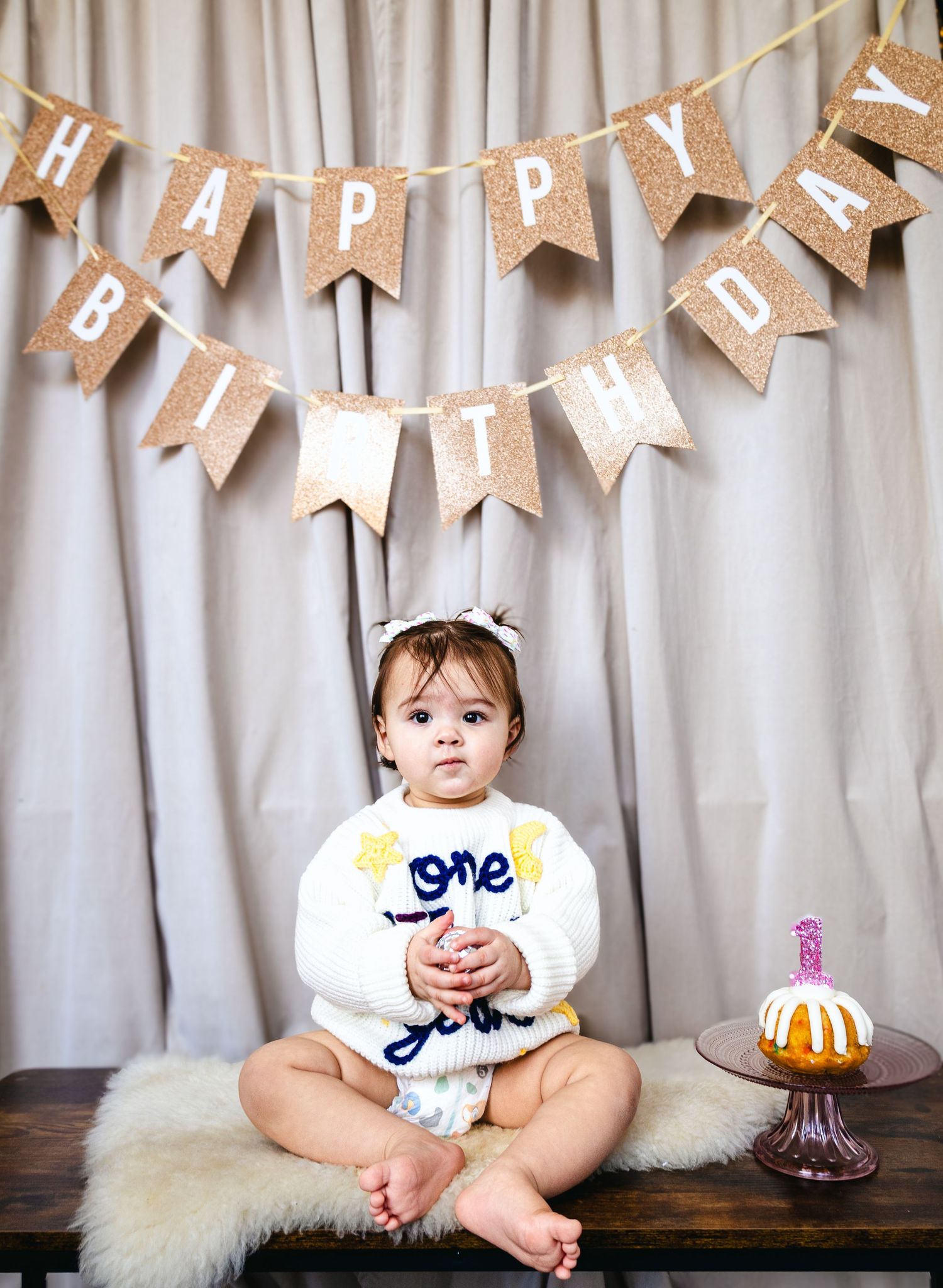 Birthday celebration setup with burlap banner and baby sitting on bench.