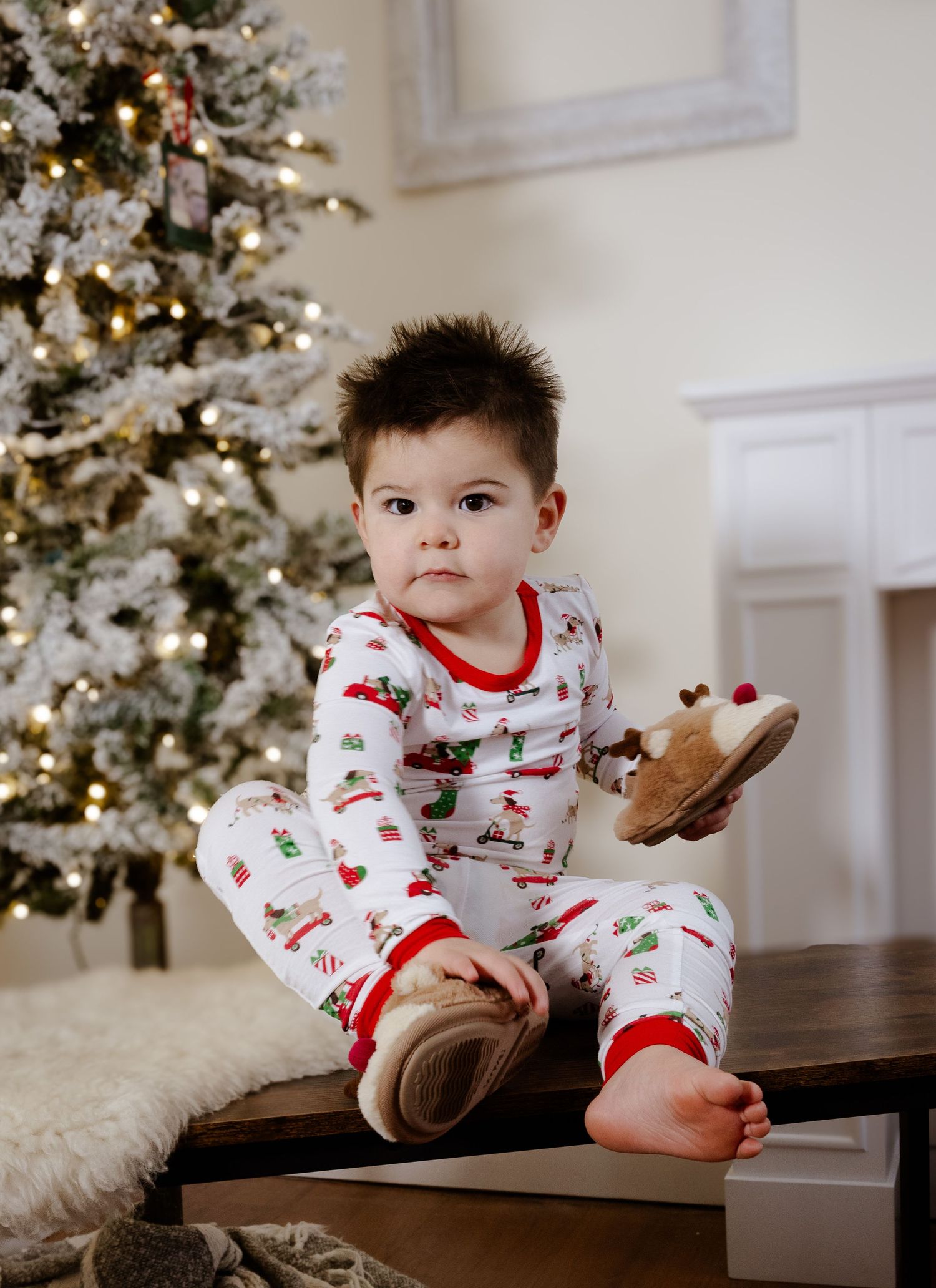 Child in holiday pajamas plays near decorated Christmas tree.