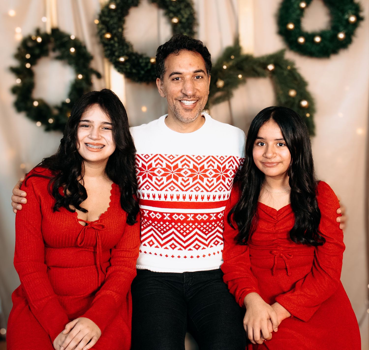Group photo with people wearing coordinated red and white holiday sweaters in front of Christmas wreaths.
