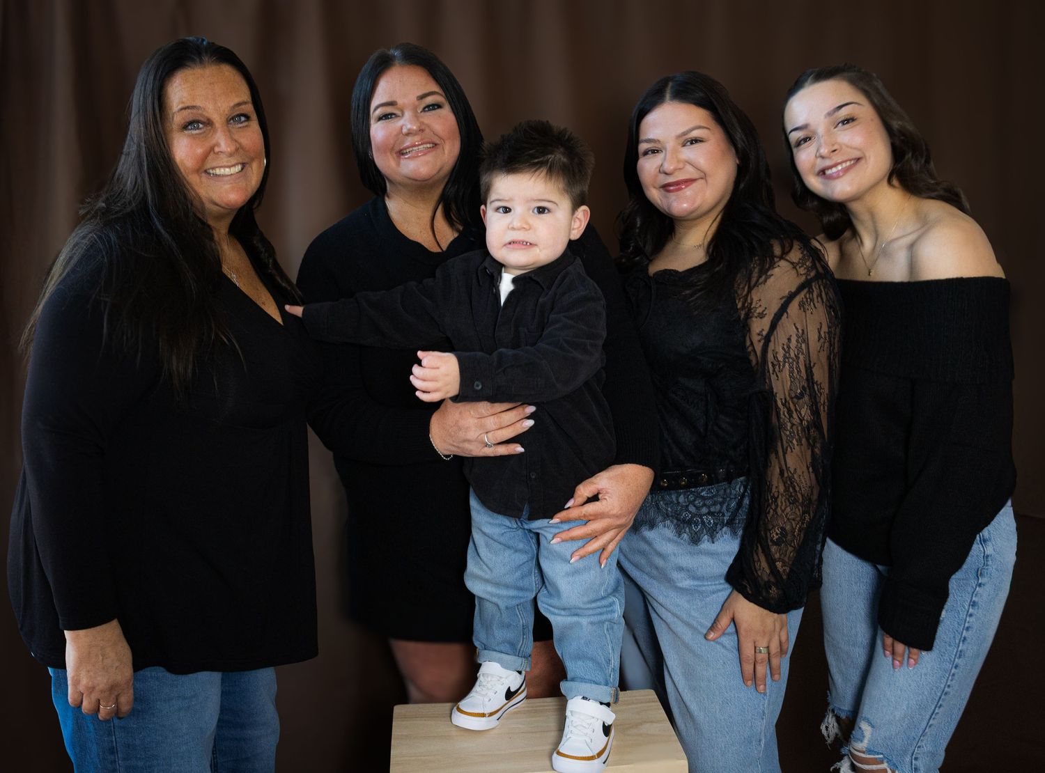 Group photo of people wearing matching black tops and jeans against dark background.