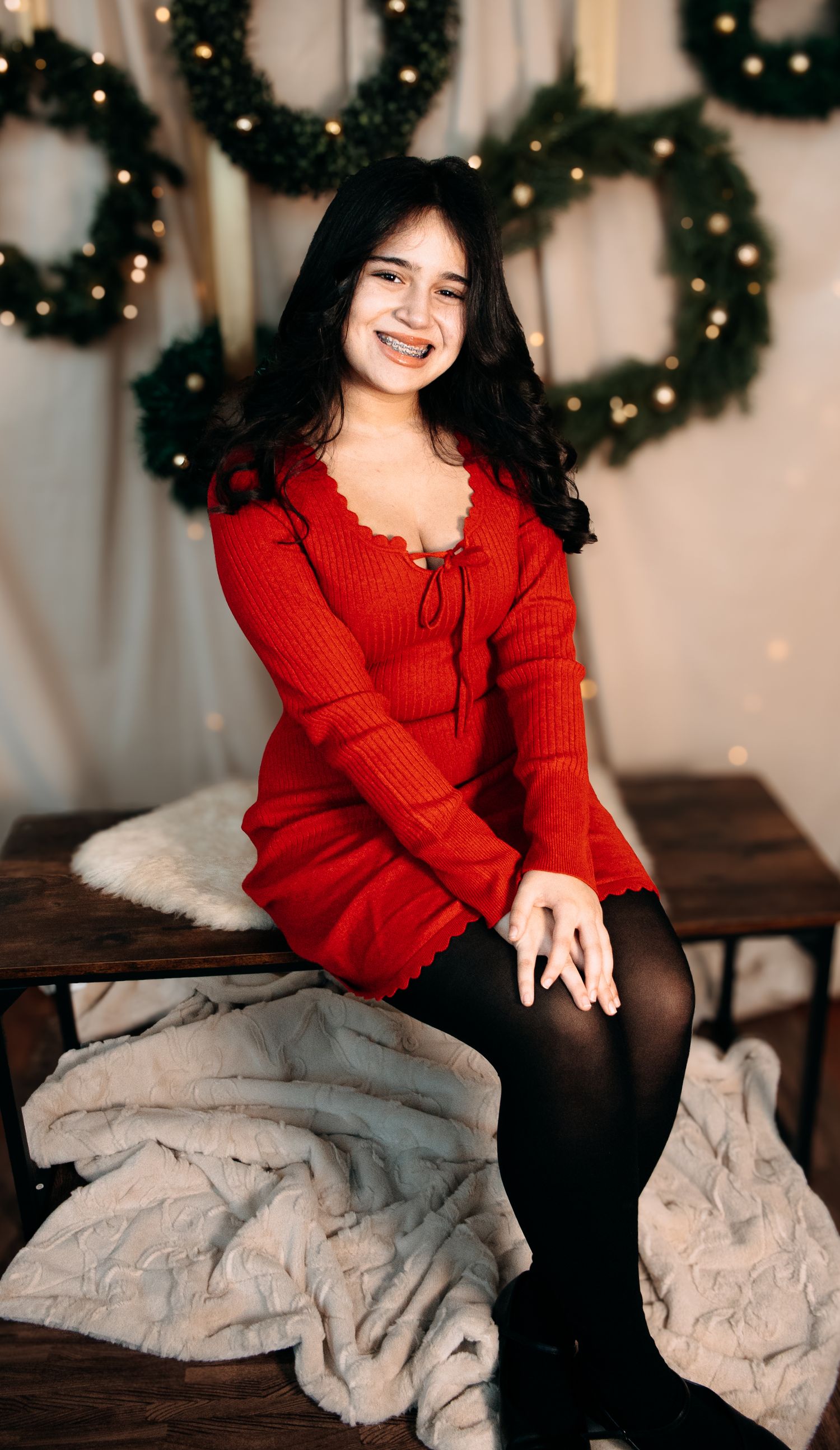 Person in red sweater sitting on bench with grey pillows in front of Christmas wreaths.